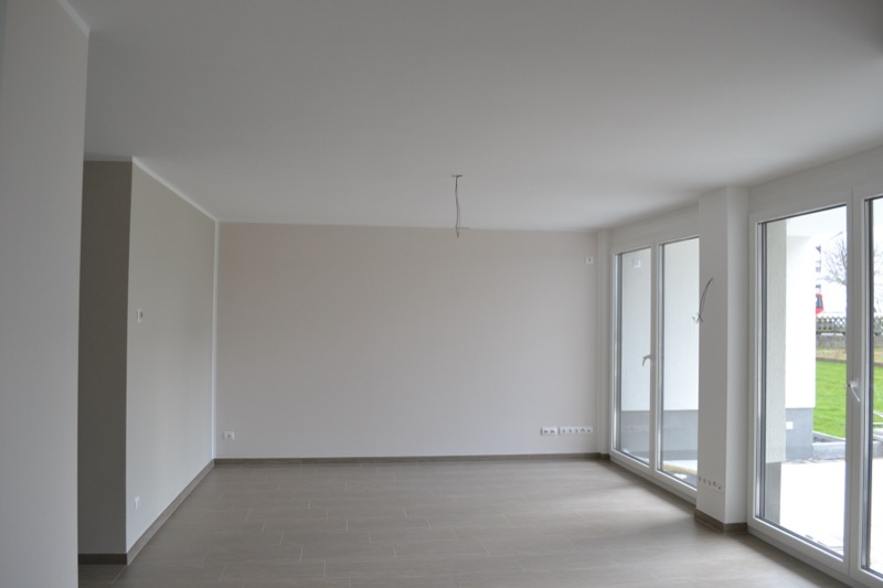 Bezugsfertiger heller Wohnraum mit bodentiefen Fenstern und Fliesenboden